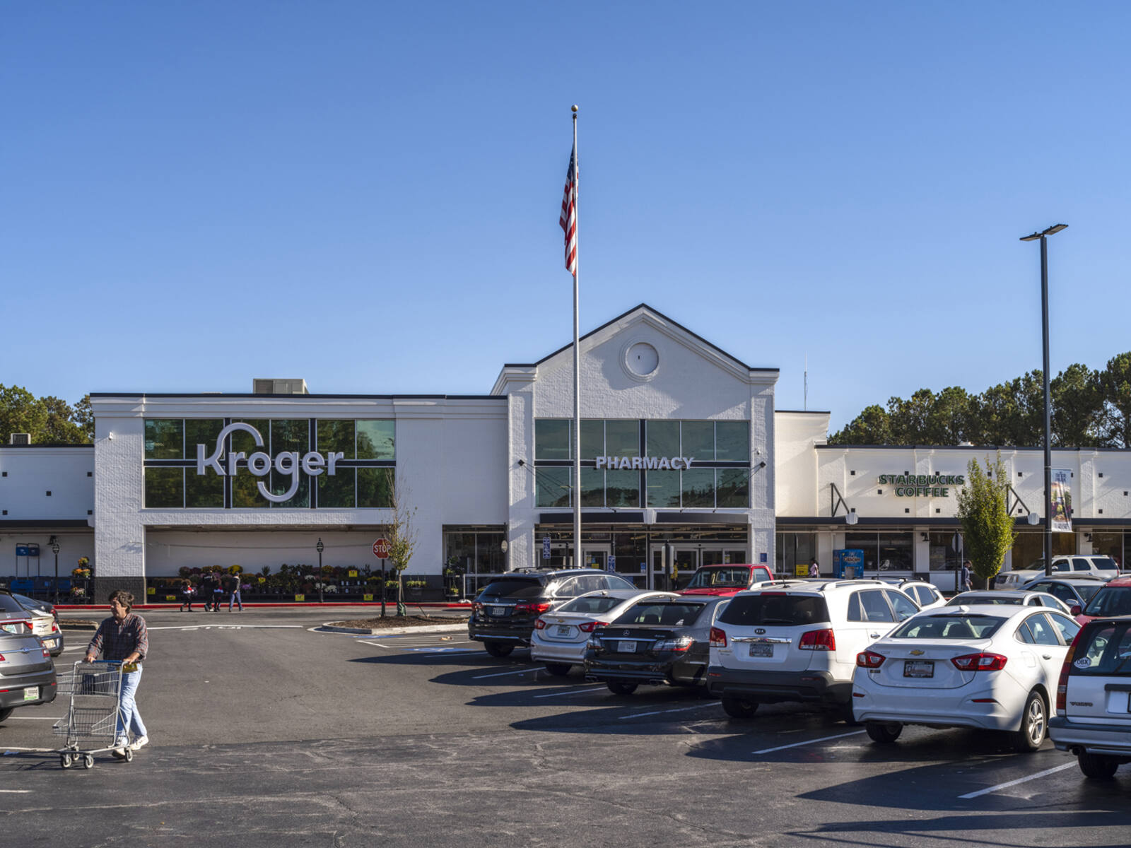 Busy parking lot for Kroger grocery with man pushing cart approaching.