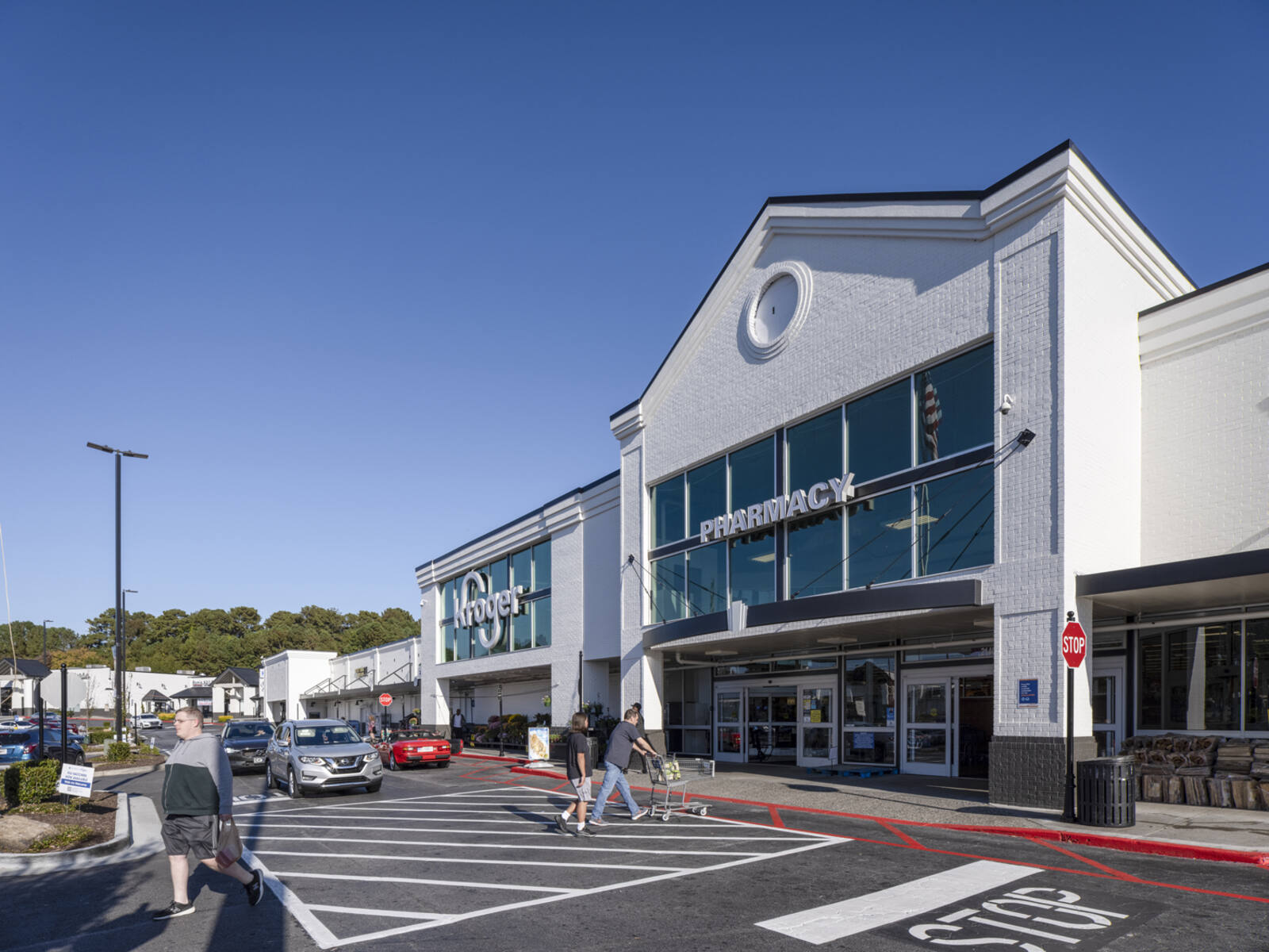 Customers with carts in crosswalk for Kroger while cars wait for pedestrians to pass.