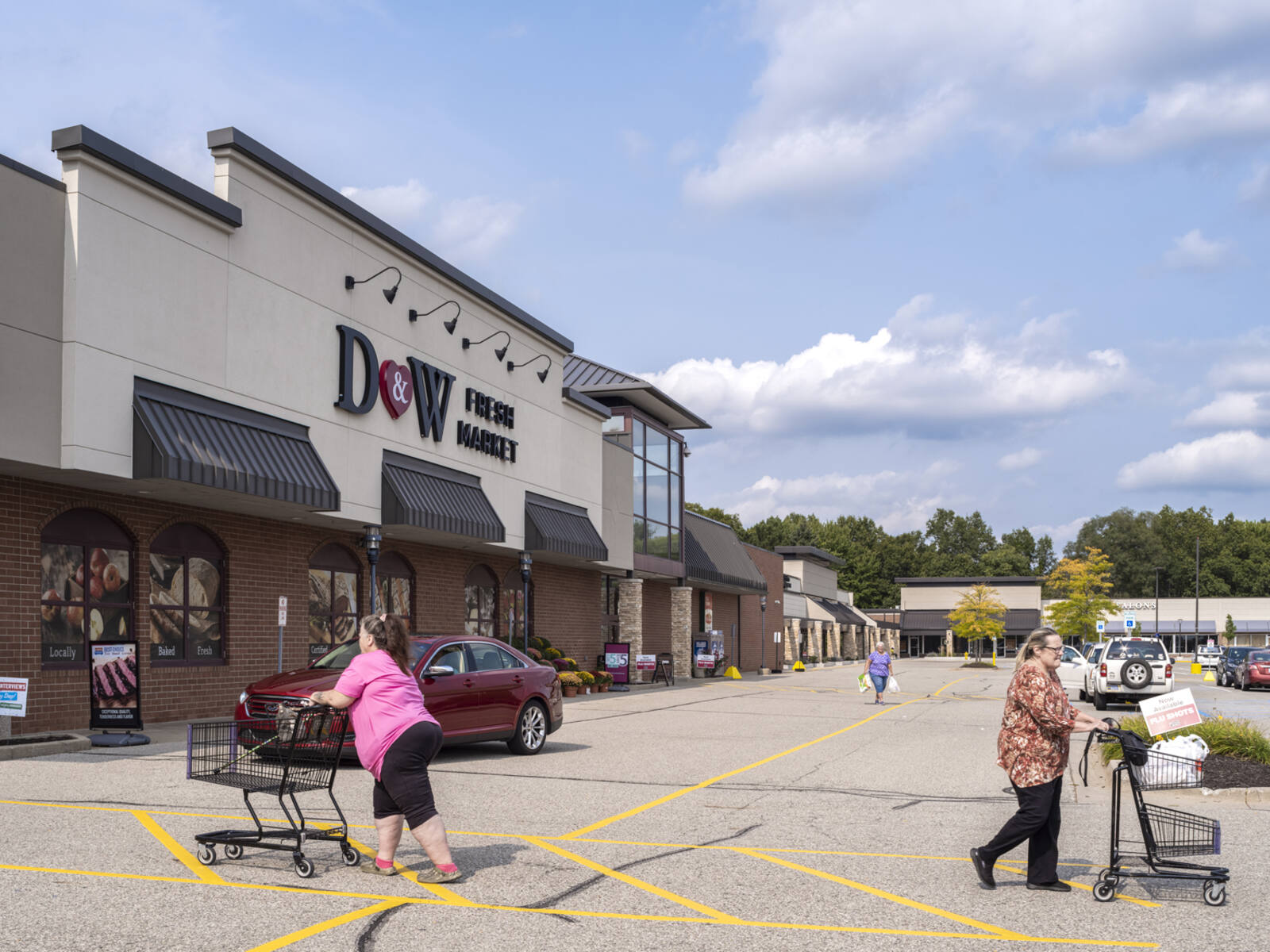 Two women with carts entering and leaving D&W Fresh Market via the parking lot.
