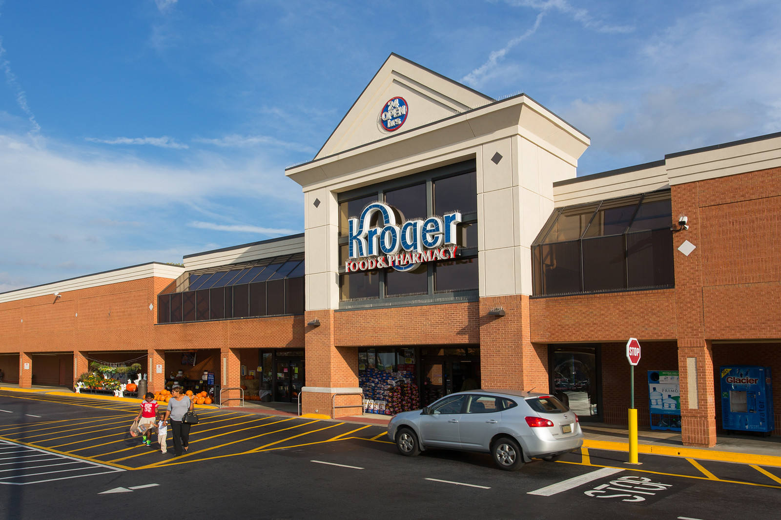 Adult and two children walk across parking lot of Kroger with a silver car parked in front