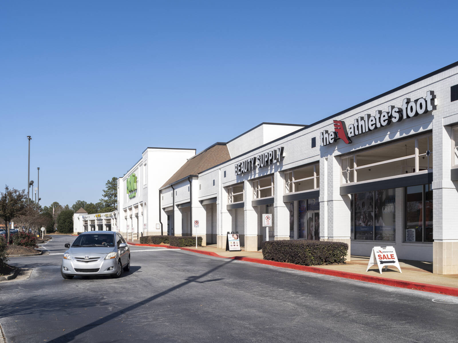 Small grey car turning on access road in front of The Athlete's Foot store.