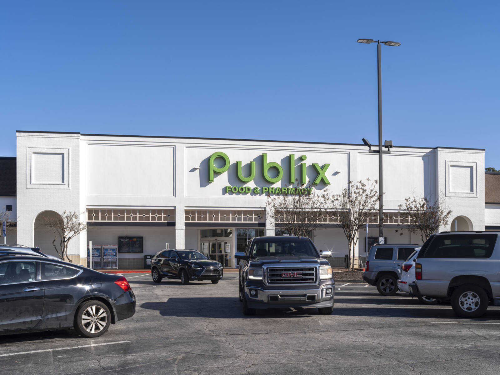 Truck driving up a row of parked cars in front of Publix grocery store.