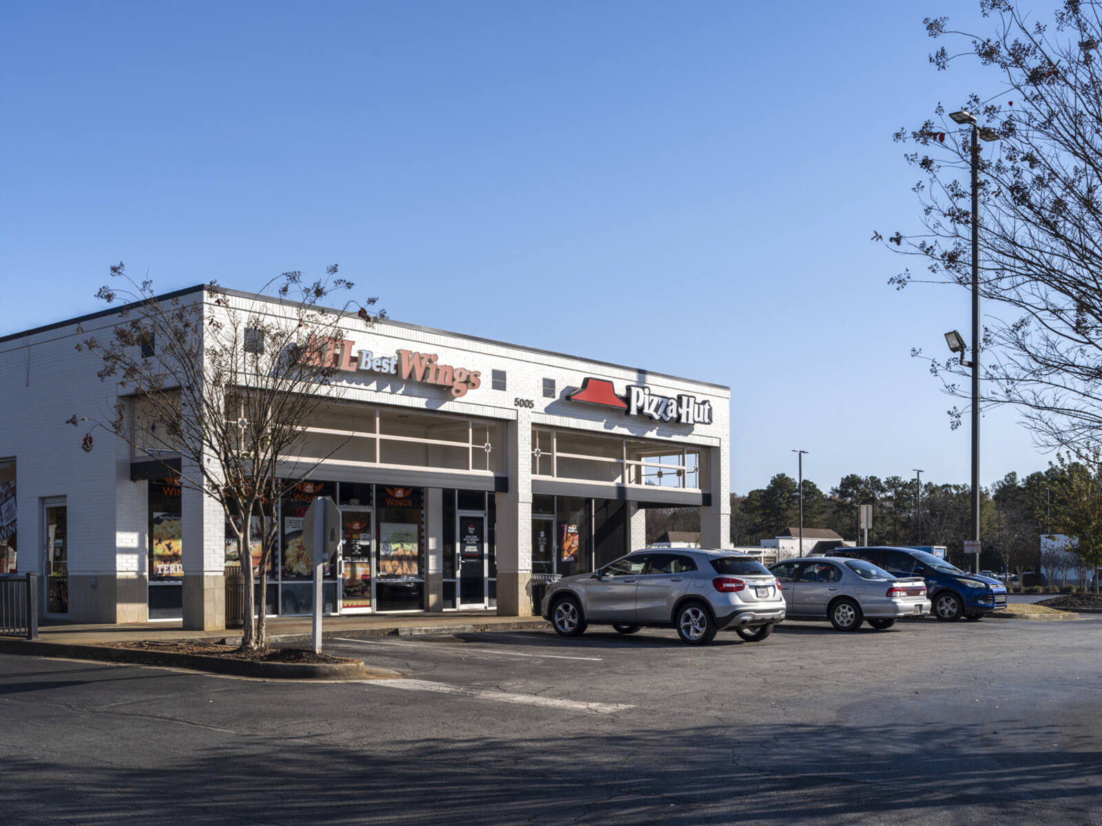 Parking lot for Pizza Hut and ATL Best Wings with trees on the side.