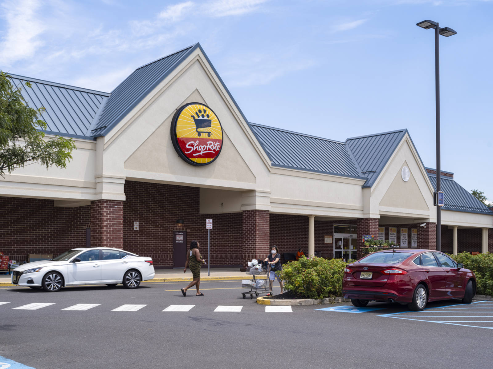 Customer with cart in front of ShopRite supermarket with shrubs and trees in parking lot at Larchmont Centre.
