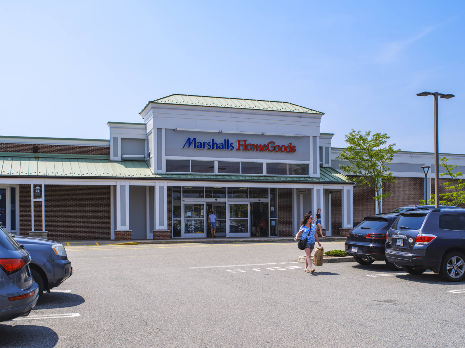 Woman in blue shirt and a shopping bag walking through the full parking lock of Marshalls HomeGoods