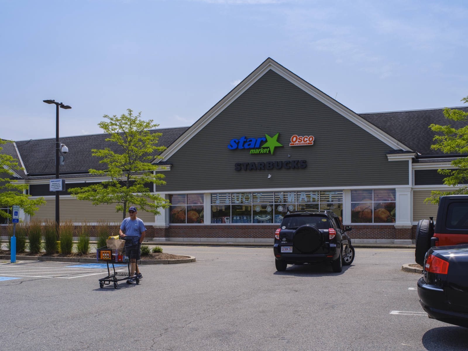 Man in blue shirt and shopping cart exiting Star Market with a black car driving past