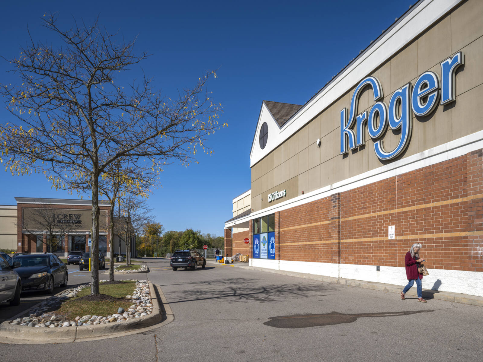 Woman leaving Kroger walking against the front façade by the parking lot.