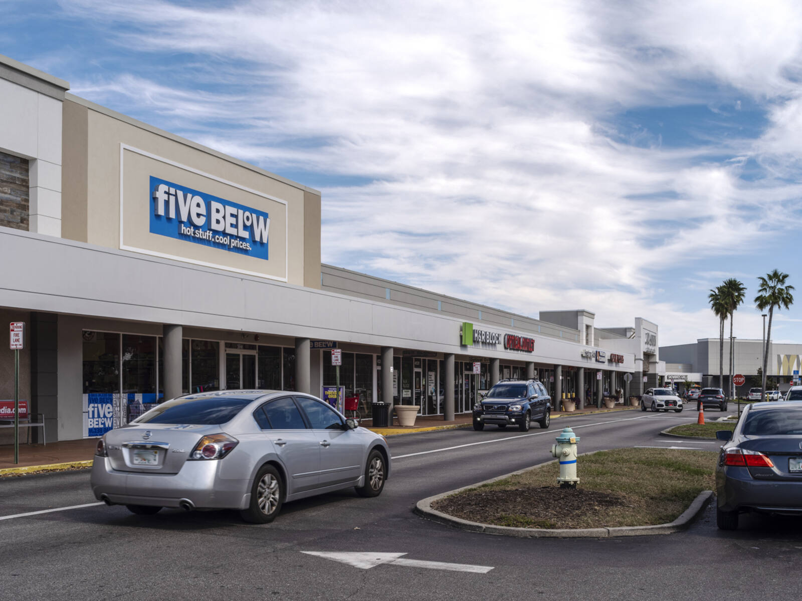 Busy road in front of Five Below at shopping center with palm trees in back.