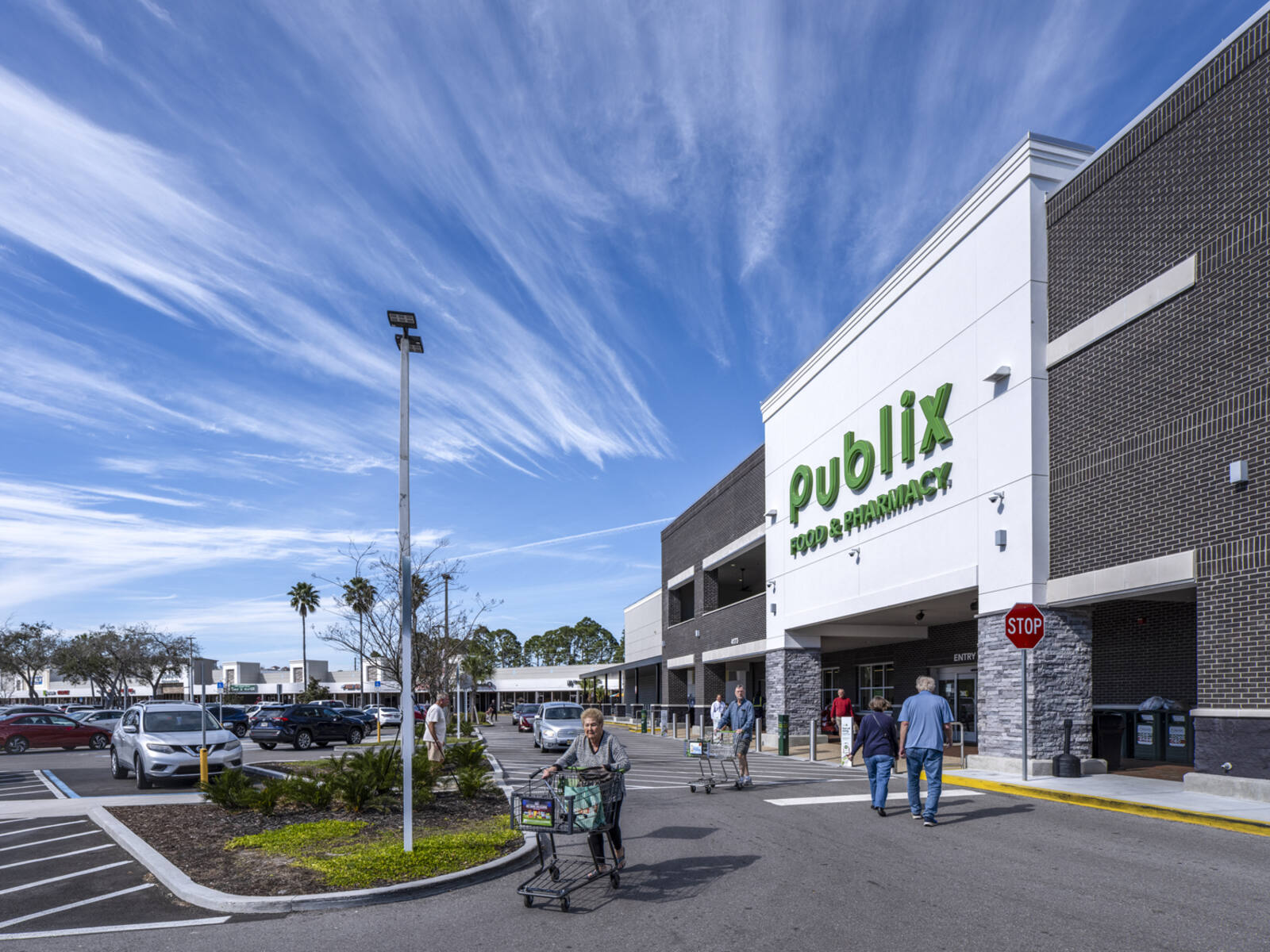 Patrons with carts entering and exiting Publix supermarket with palm trees in the back.