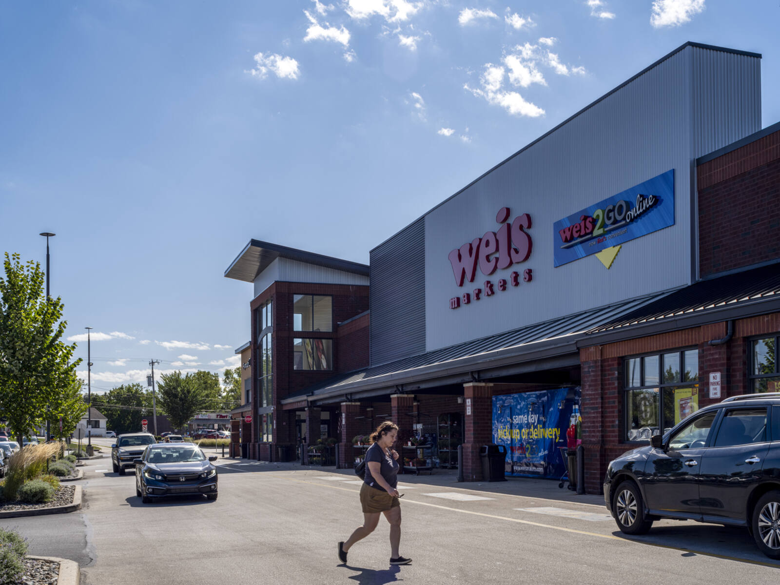 Woman in crosswalk of Weis supermarket with cars on both sides of road.