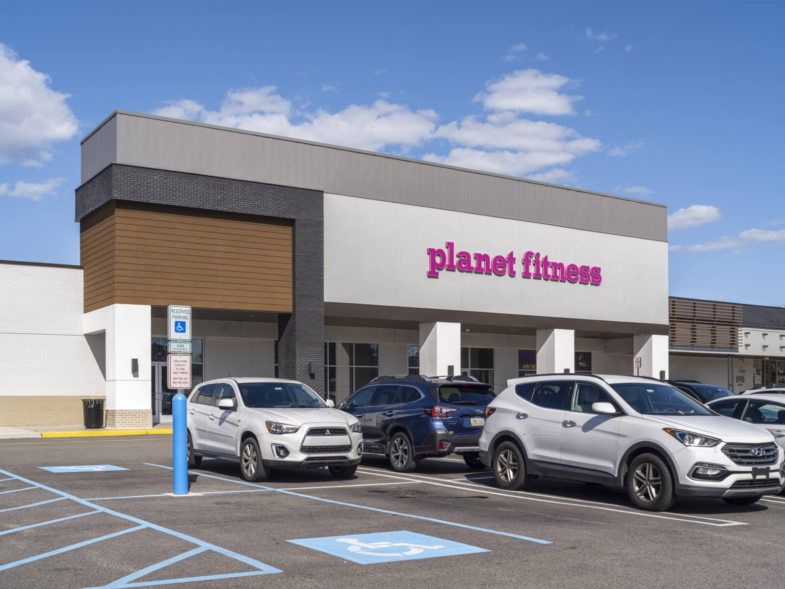 Cars in busy parking lot at Planet Fitness storefront.