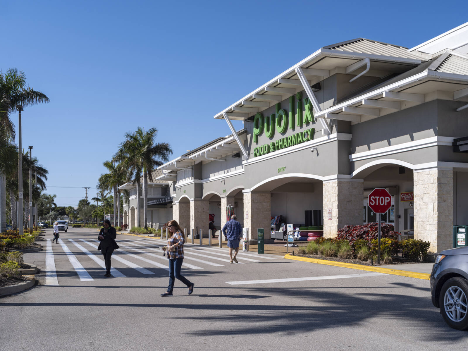 People in crosswalk for Publix store with palm trees on sidewalk.