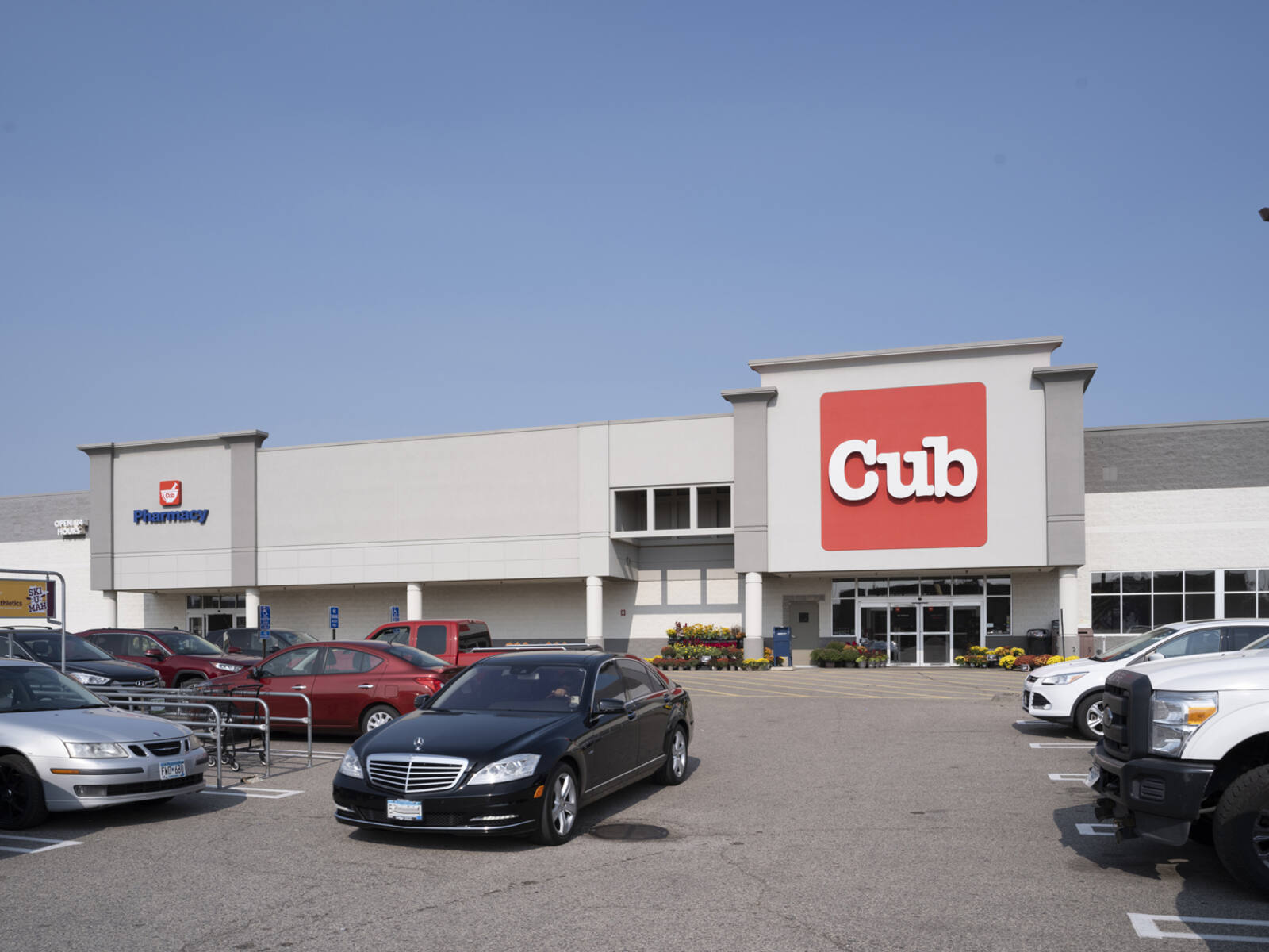 Black sedan amidst busy parking lot in front of Cub Foods and Pharmacy.