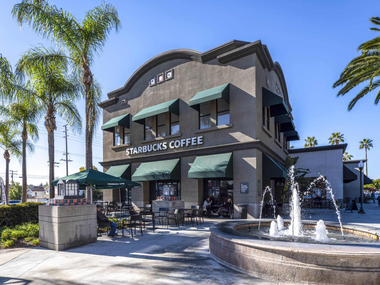 Customers enjoying outdoor seating with palm trees and a fountain at the Starbucks at Brea Gateway.