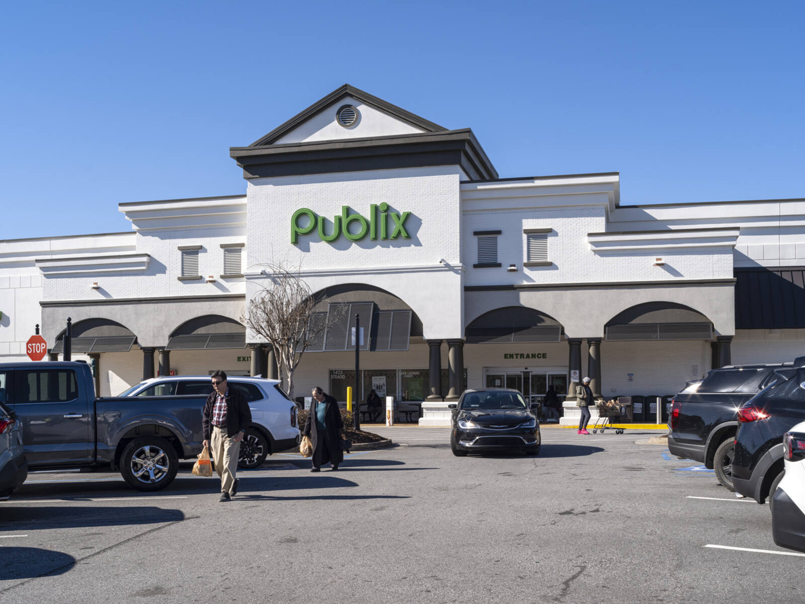 Busy aisle of parking lot at Publix with patrons carrying bags and car approaching.