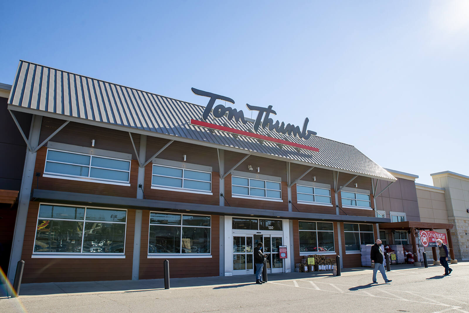 Shoppers entering Tom Thumb grocery store on a sunny day.