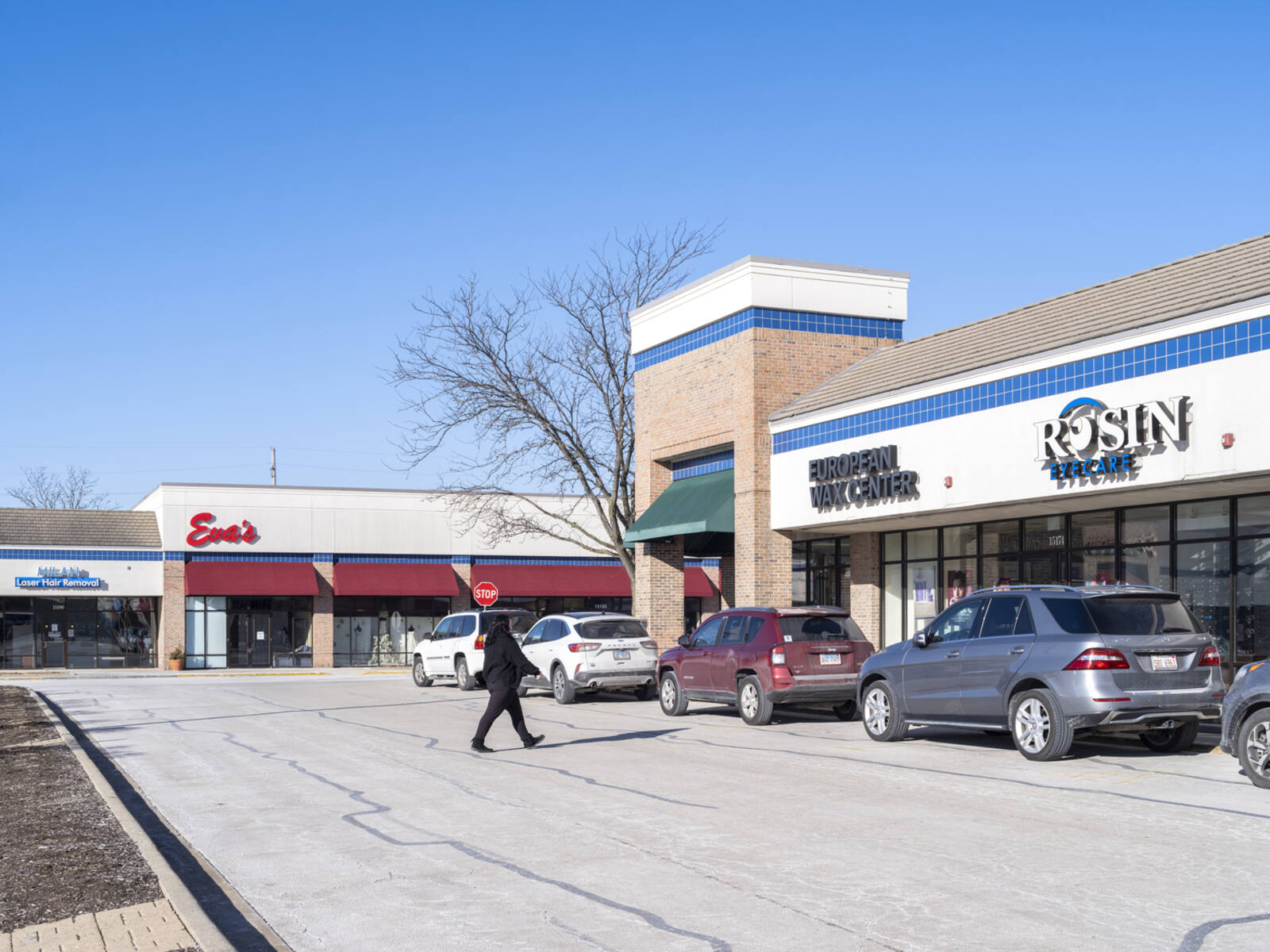 Person in black walking towards Rosin Eyecare at Ravinia Plaza shopping center