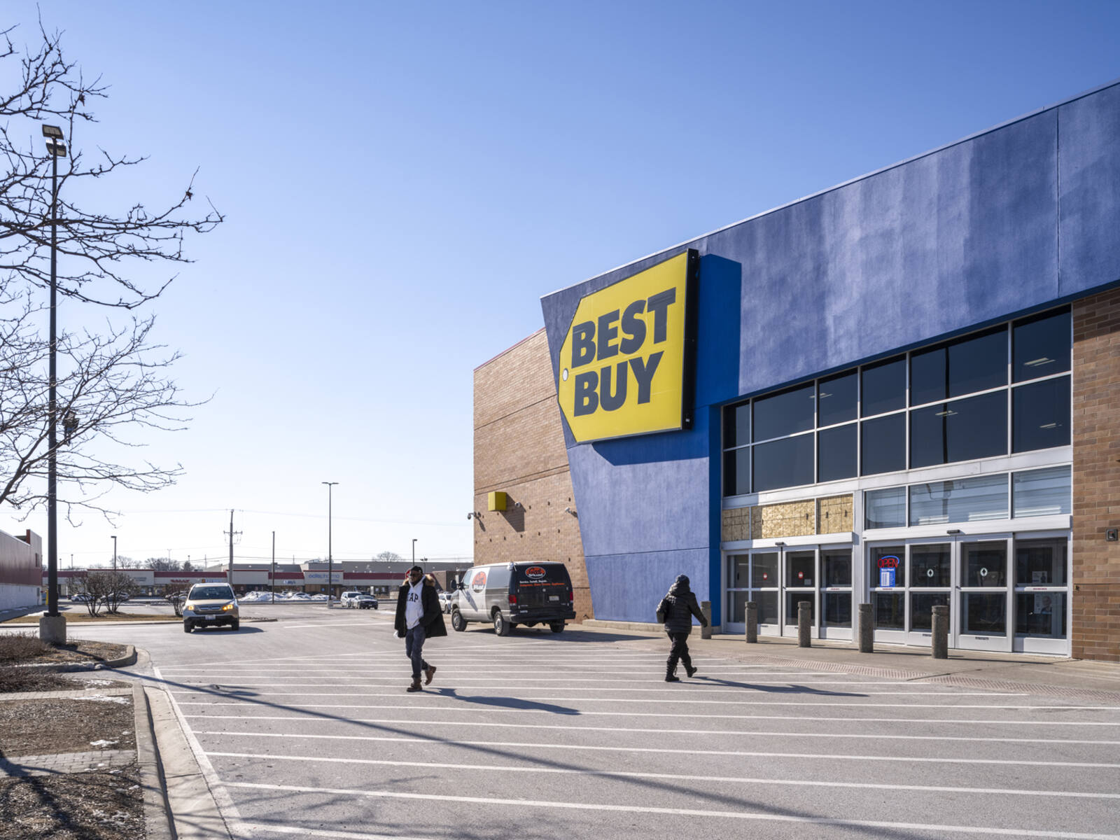 Customers and cars on intersection in front of Best Buy retail store.