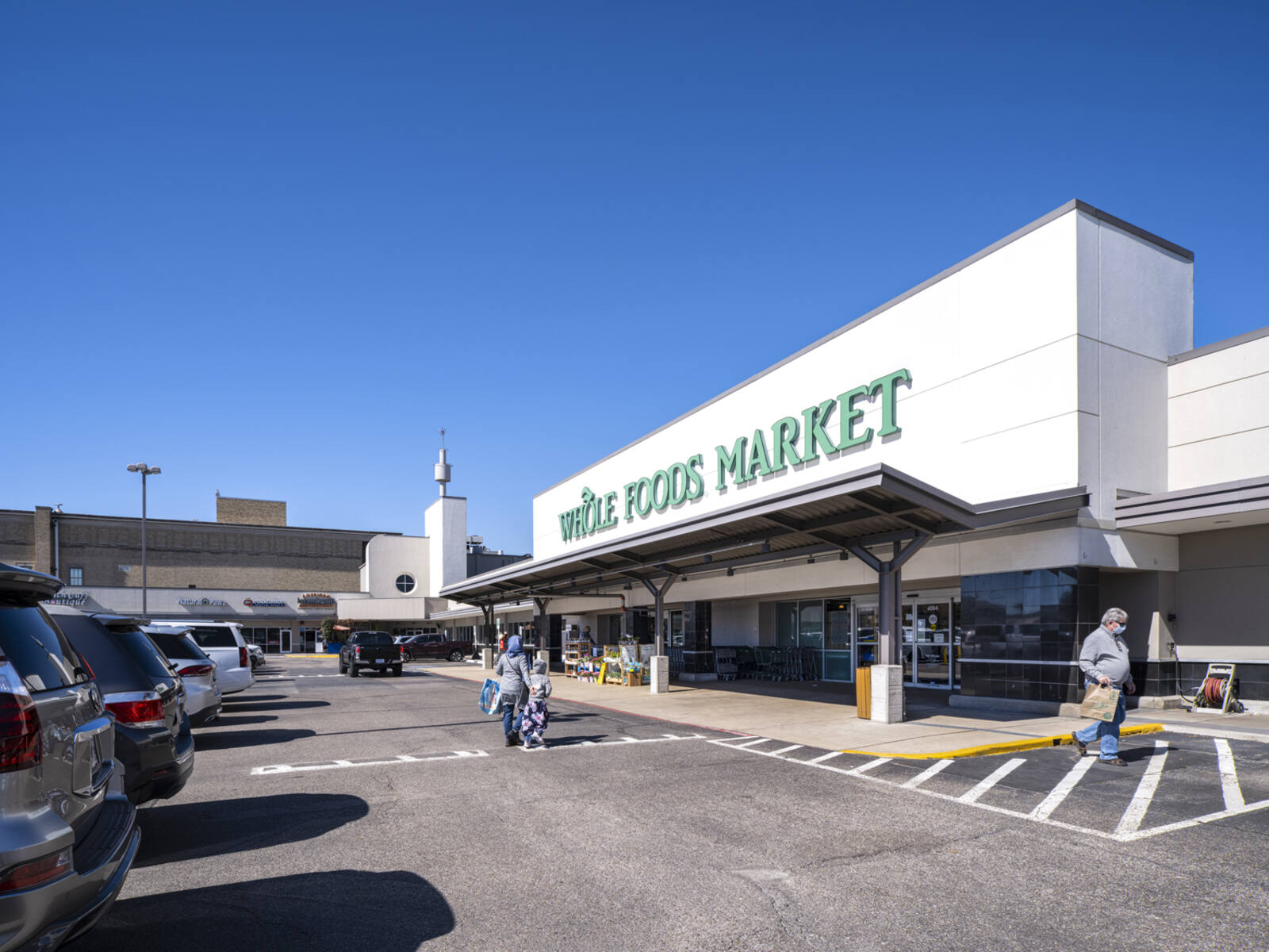 Family entering Whole Foods Market through parking lot in West U Marketplace.