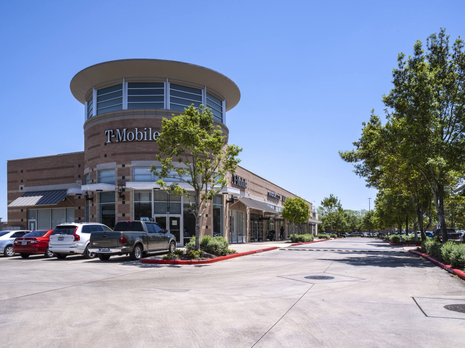 T-Mobile store with trees at entrance and side of parking lot.