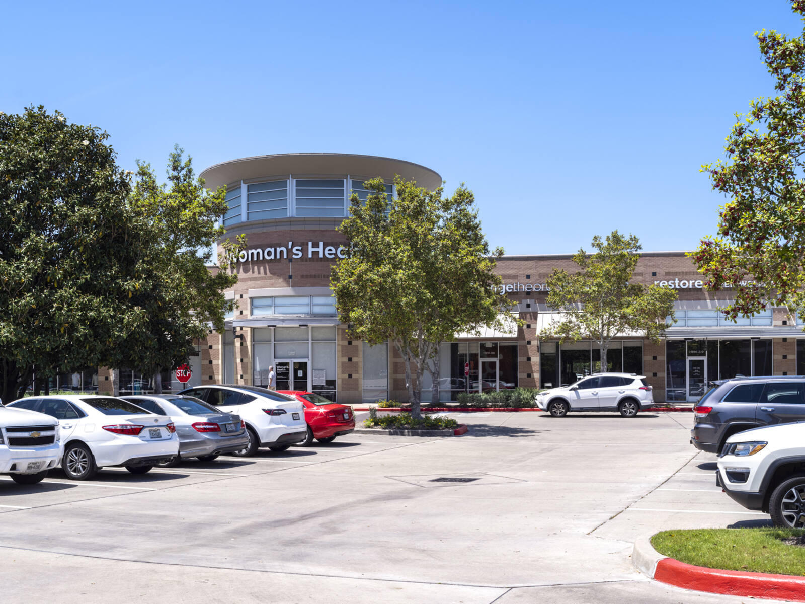 Woman's Health center with trees and rows of parked car at entrance.