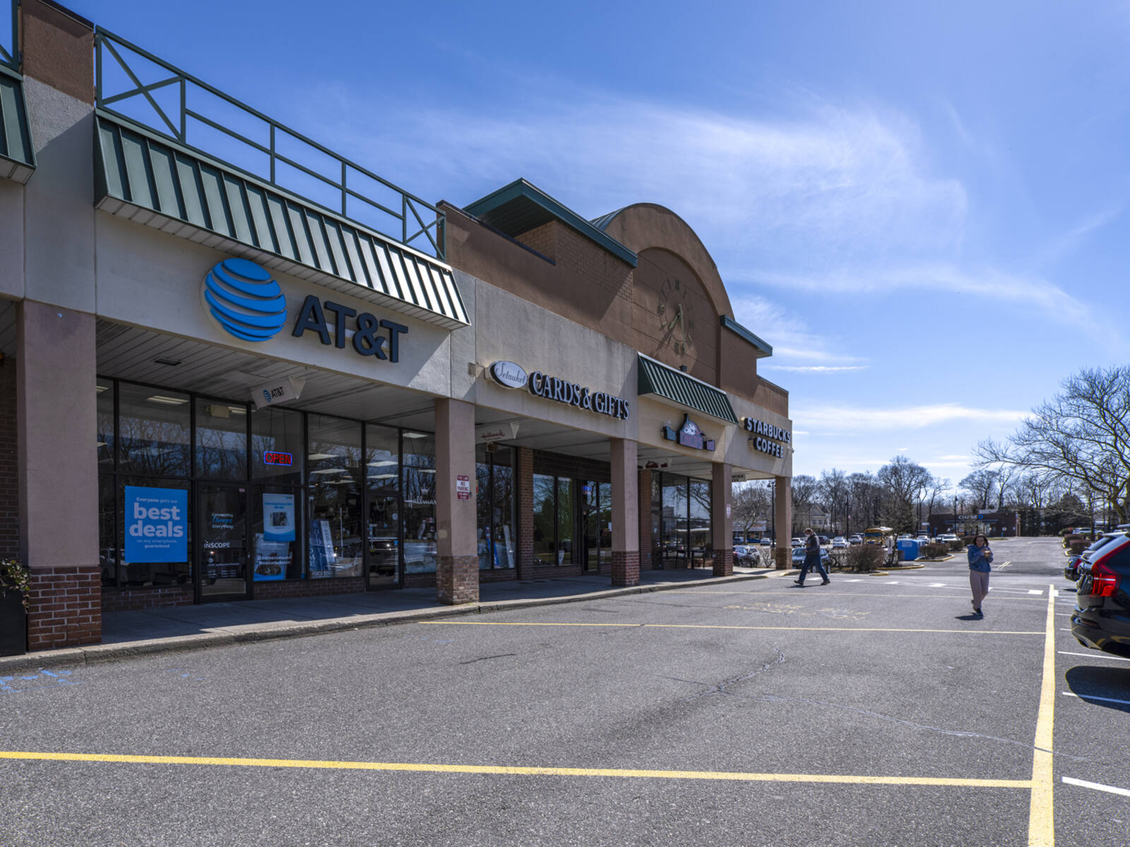 Pedestrians cross access road in front of shopping center stores like AT&T.