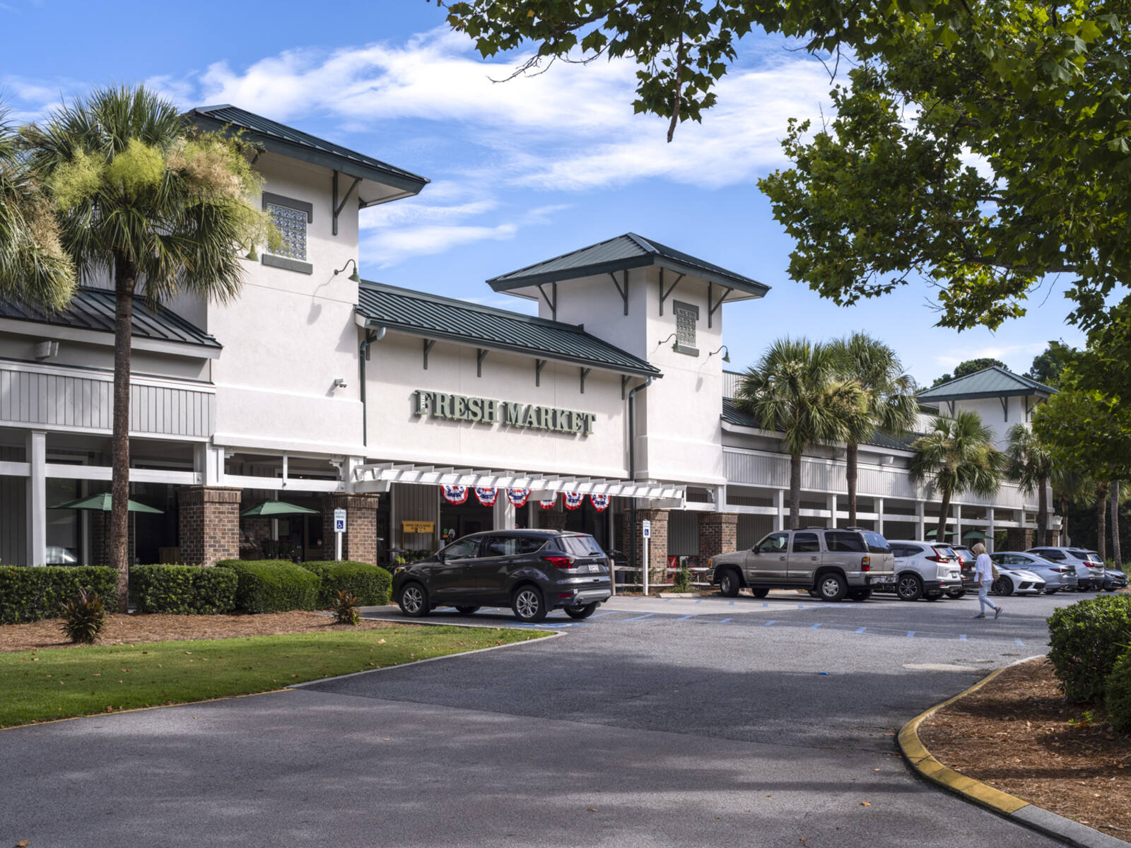 Palm trees and greenery surround busy parking lot in front of Fresh Market.