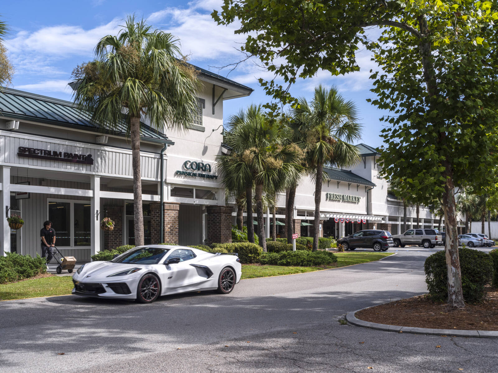 White sports car and palm trees in front of shops at Fresh Market Shoppes shopping center.