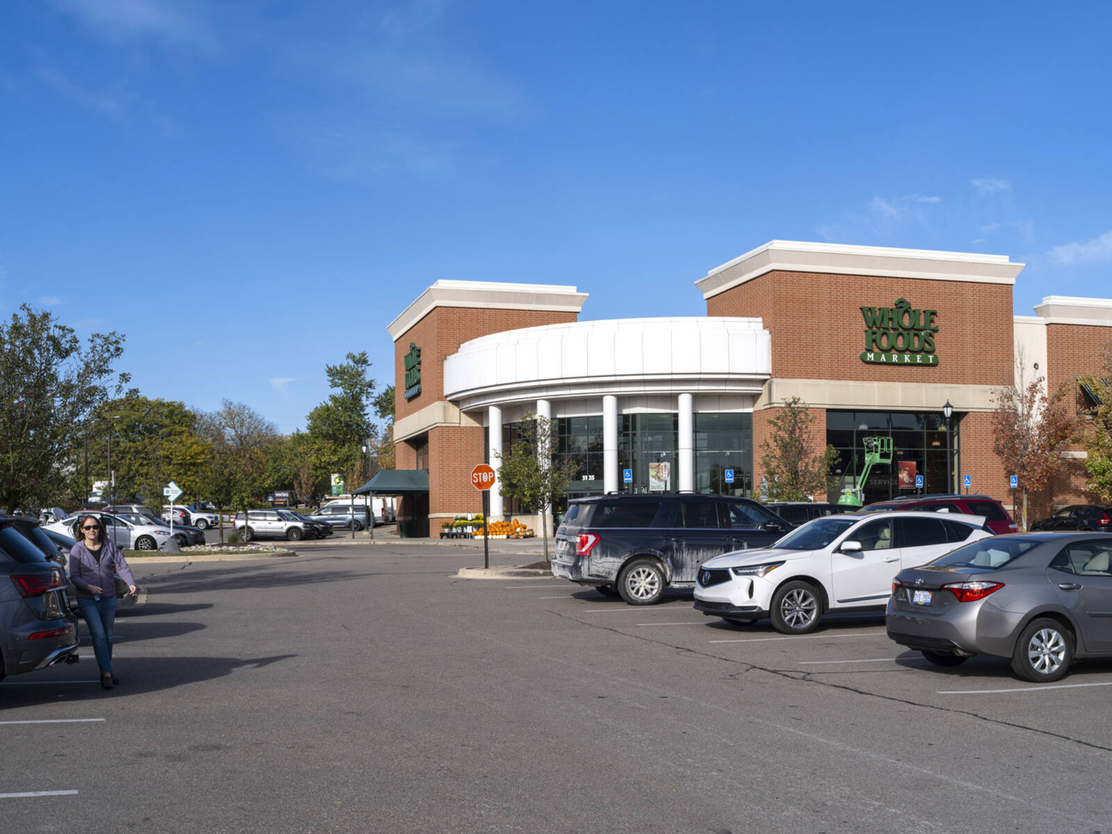 Whole Foods Market with rows of cars in parking lot on sides and patron walking on the left.