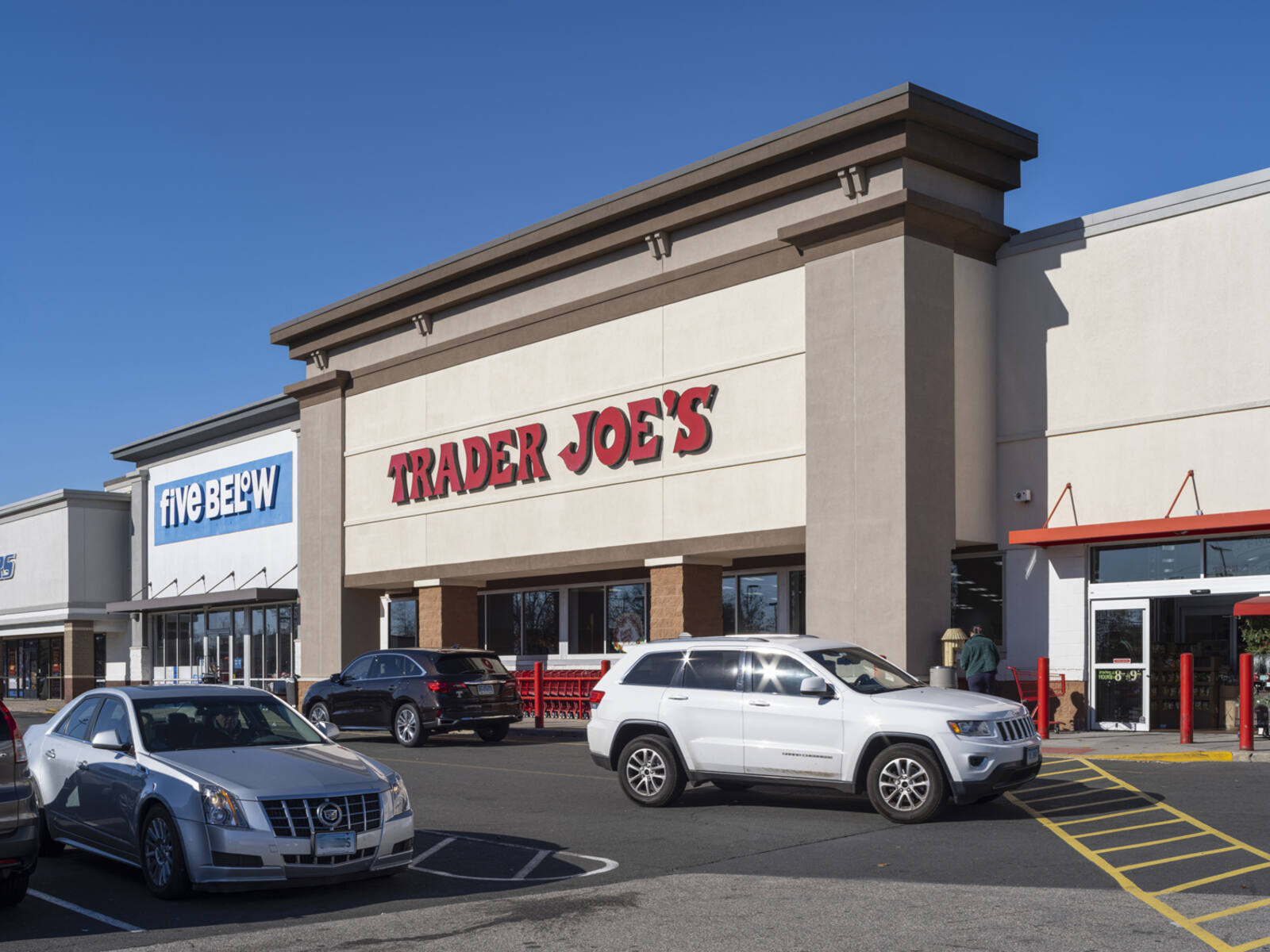 Cars passing on road in front of Trader Joe's and Five Below stores.