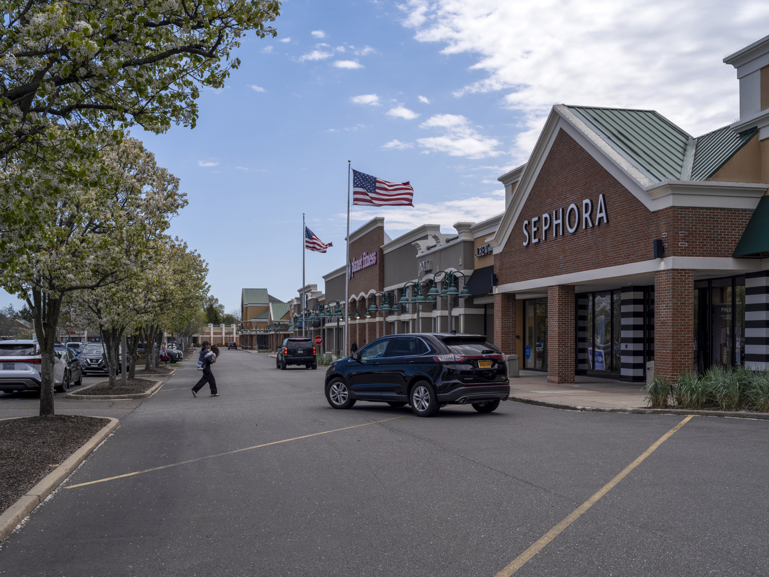 Cars and people crossing road in front of Sephora with tree on the left.