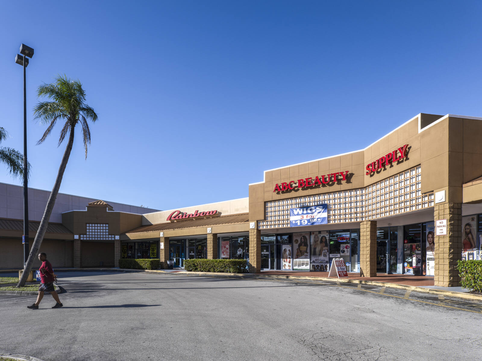 ABC Beauty Supply with pedestrian in crosswalk and Rainbow department store in background.