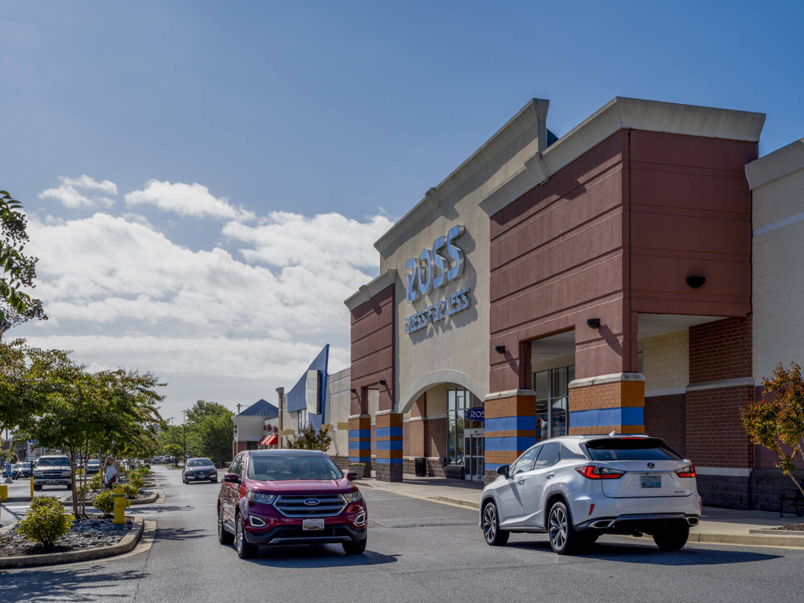 Ross Dress for Less with a red and a white car passing at storefront.