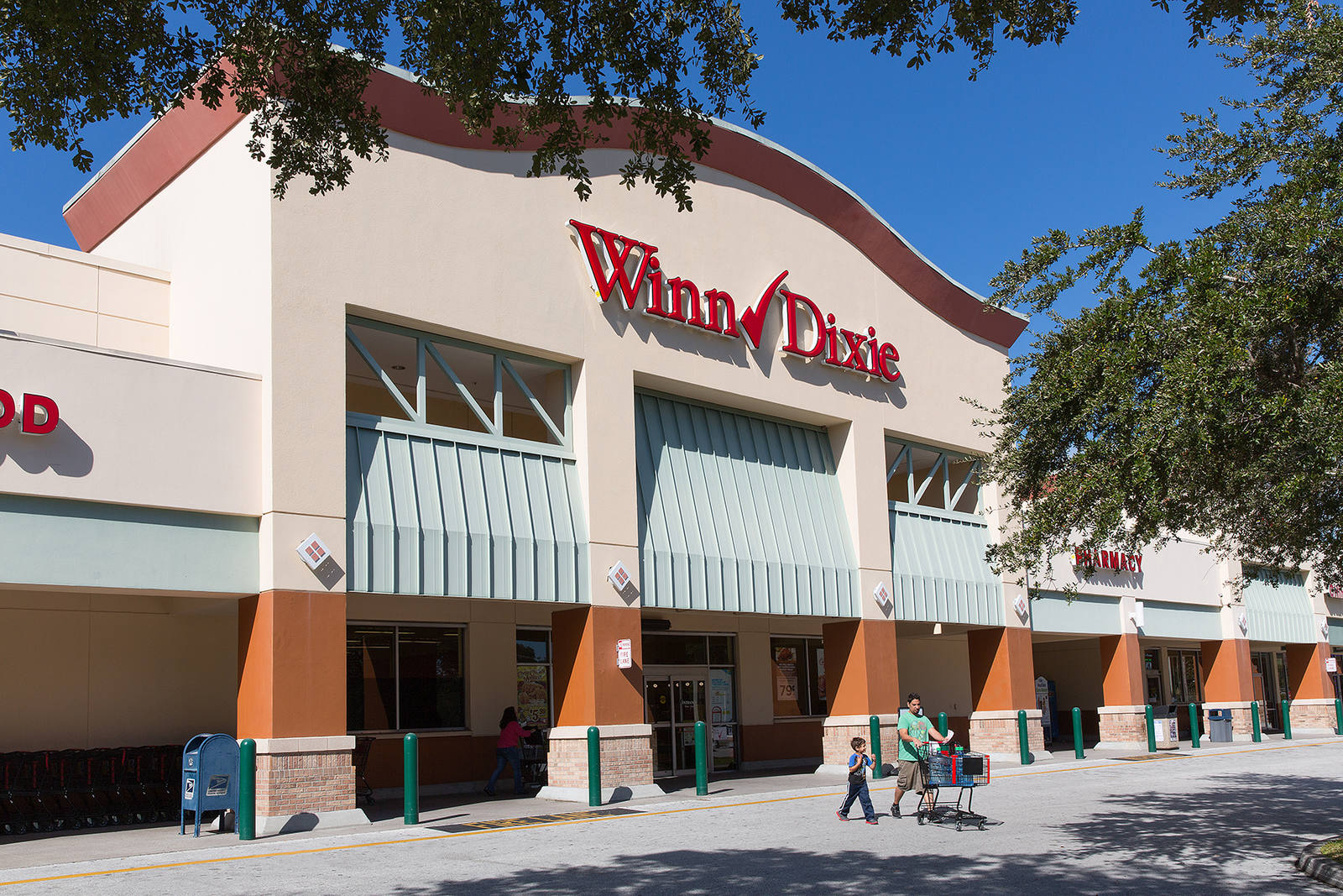 Winn Dixie supermarket with trees and customers with cart at Lake St. Charles shopping center.