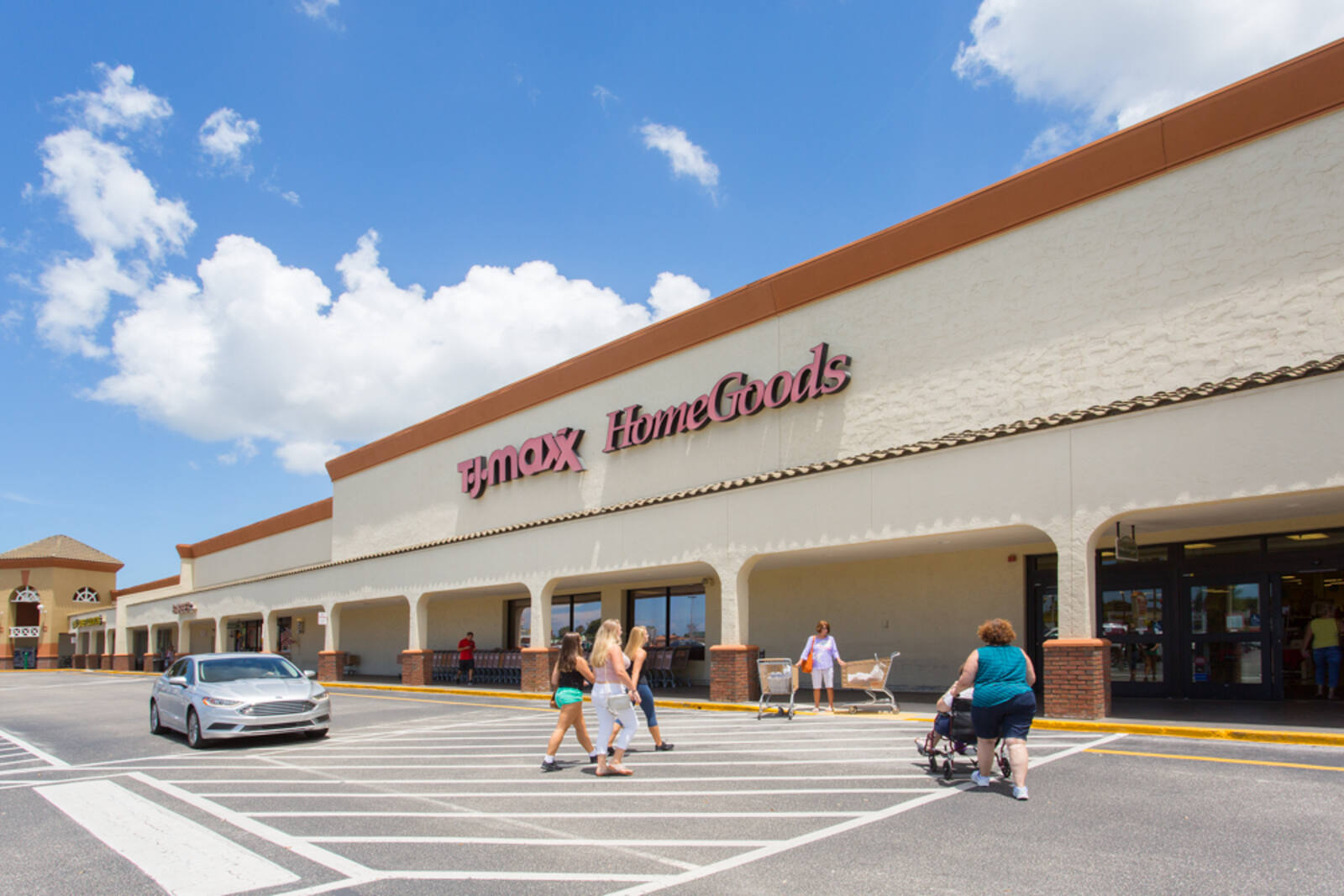 People walking into the entrance of T.J. Maxx and Home Goods and a silver car passing by