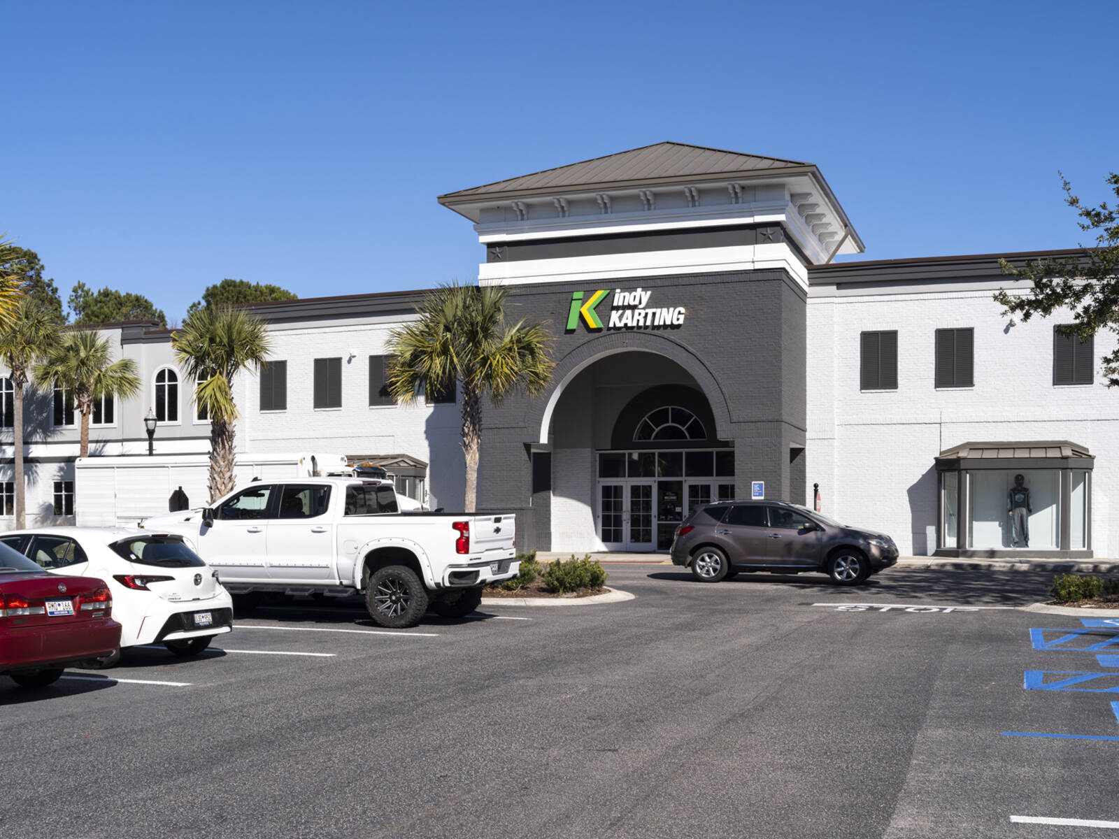 Indy Karting storefront with palm trees and aisle of cars in lot.