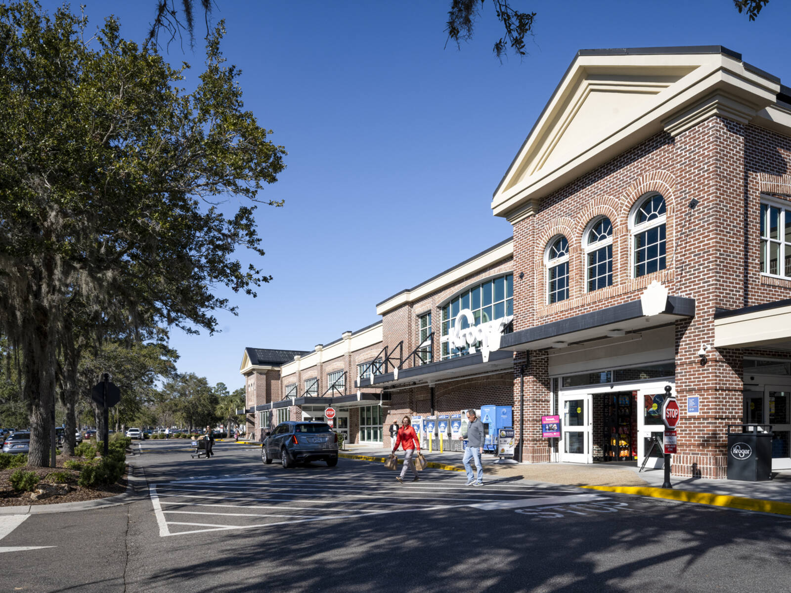 Patrons in crosswalk of Kroger with large tree on left.