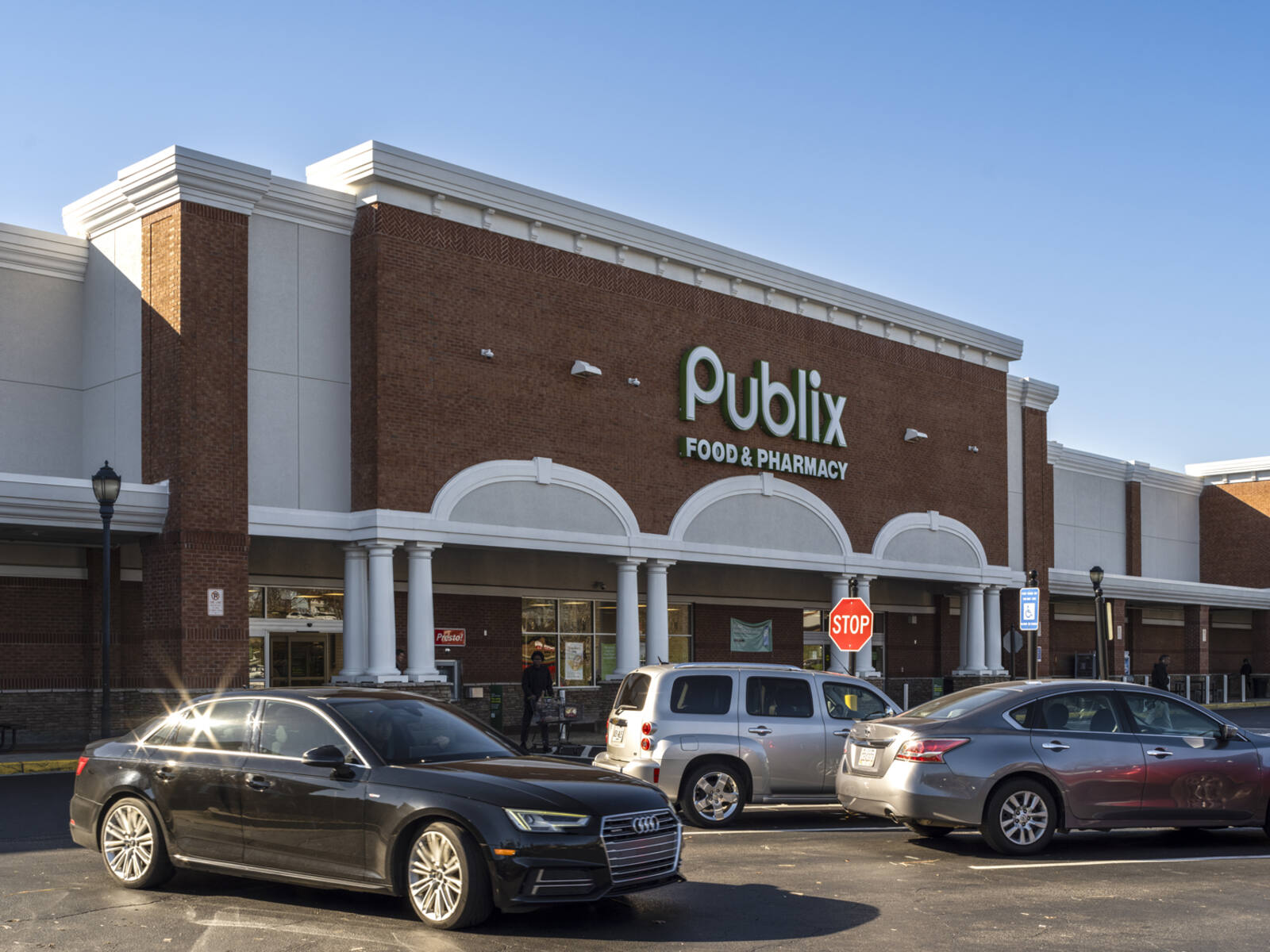 Busy parking lot in front of Publix grocer with dark car in foreground.