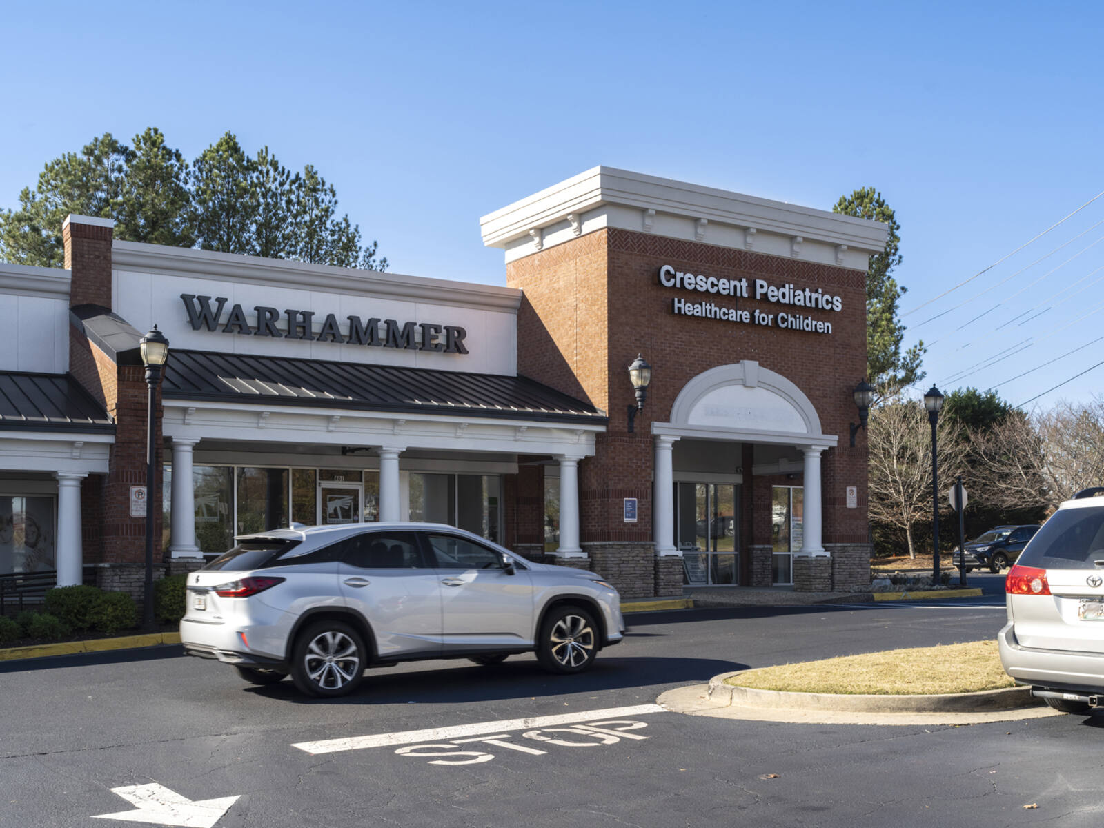 Grey SUV passing Crescent Pediatrics on road in shopping center.