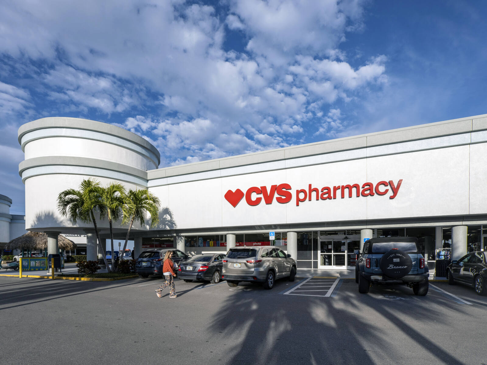 CVS Pharmacy with woman approaching parking lot with palm trees on left.