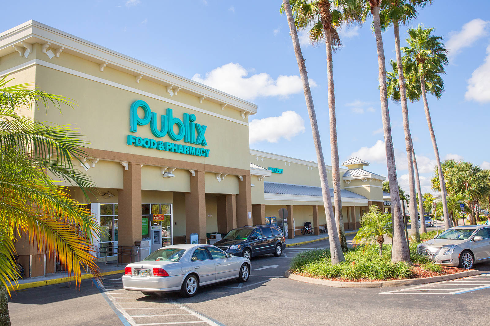 Cars pulled up to the front of Publix supermarket with palm trees and shrubs.