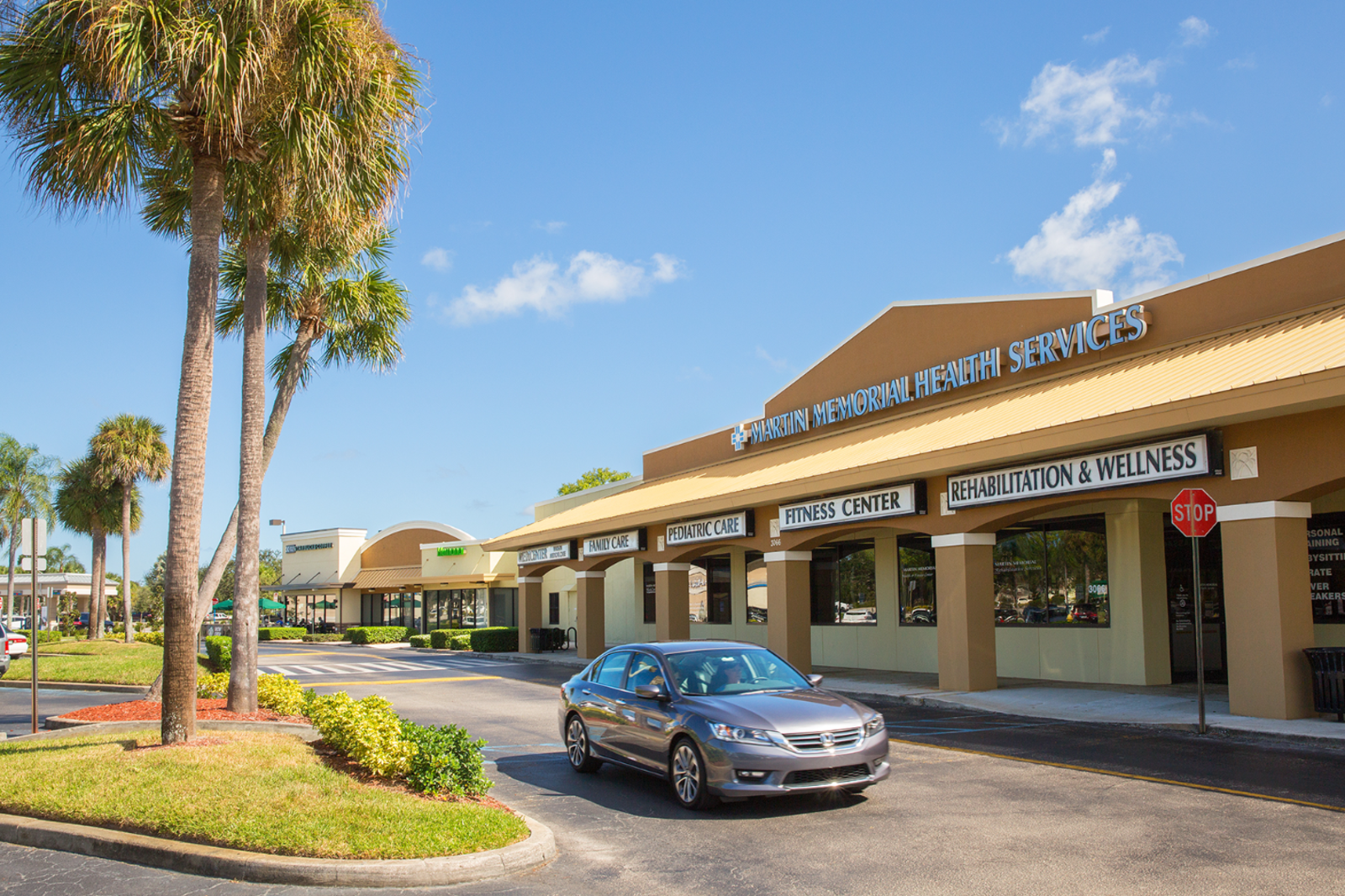 Car passed palm trees on access road in shopping center.