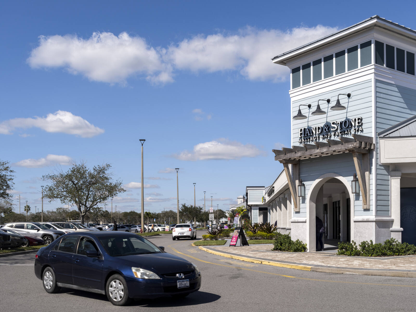 Hand & Stone spa with busy parking lot and trees behind store.