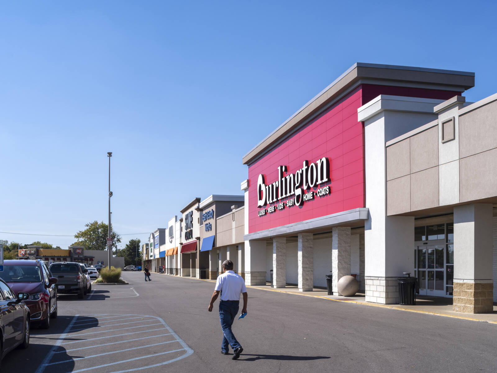 Man walking in front of Burlington store towards parking lot.