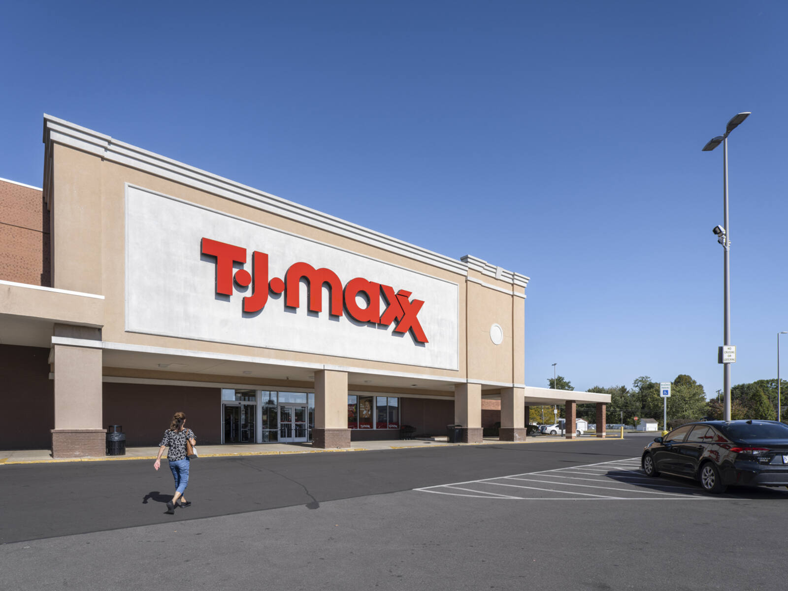 Woman approaches TJ Maxx from parking lot with trees in the background.
