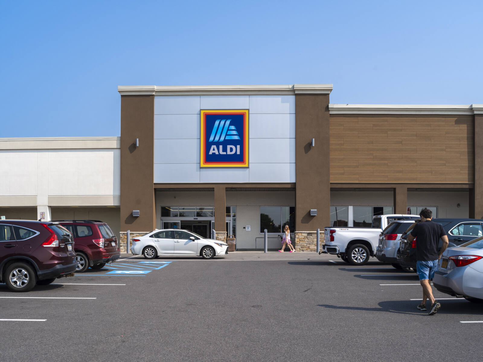Busy parking lot in front of Aldi with cars and people approaching storefront.