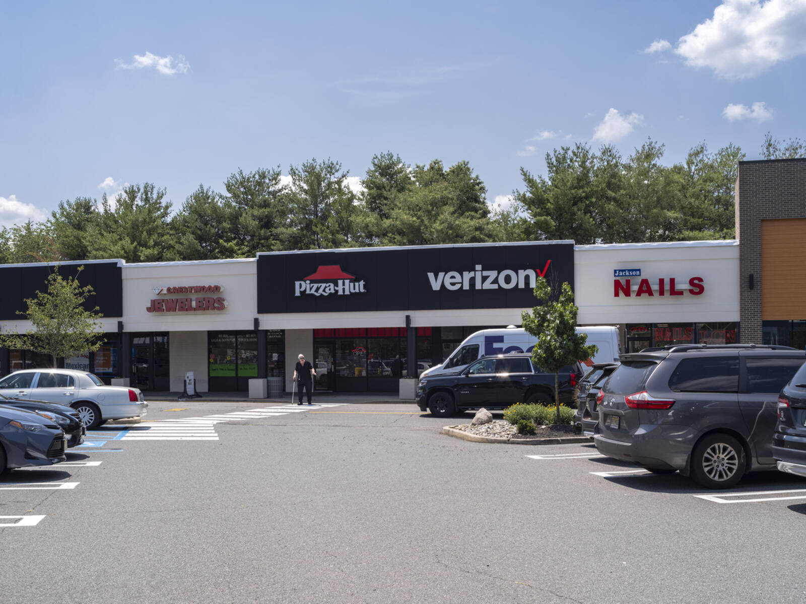 Pizza-Hut and Verizon stores with trees behind them and patron in cross-walk.