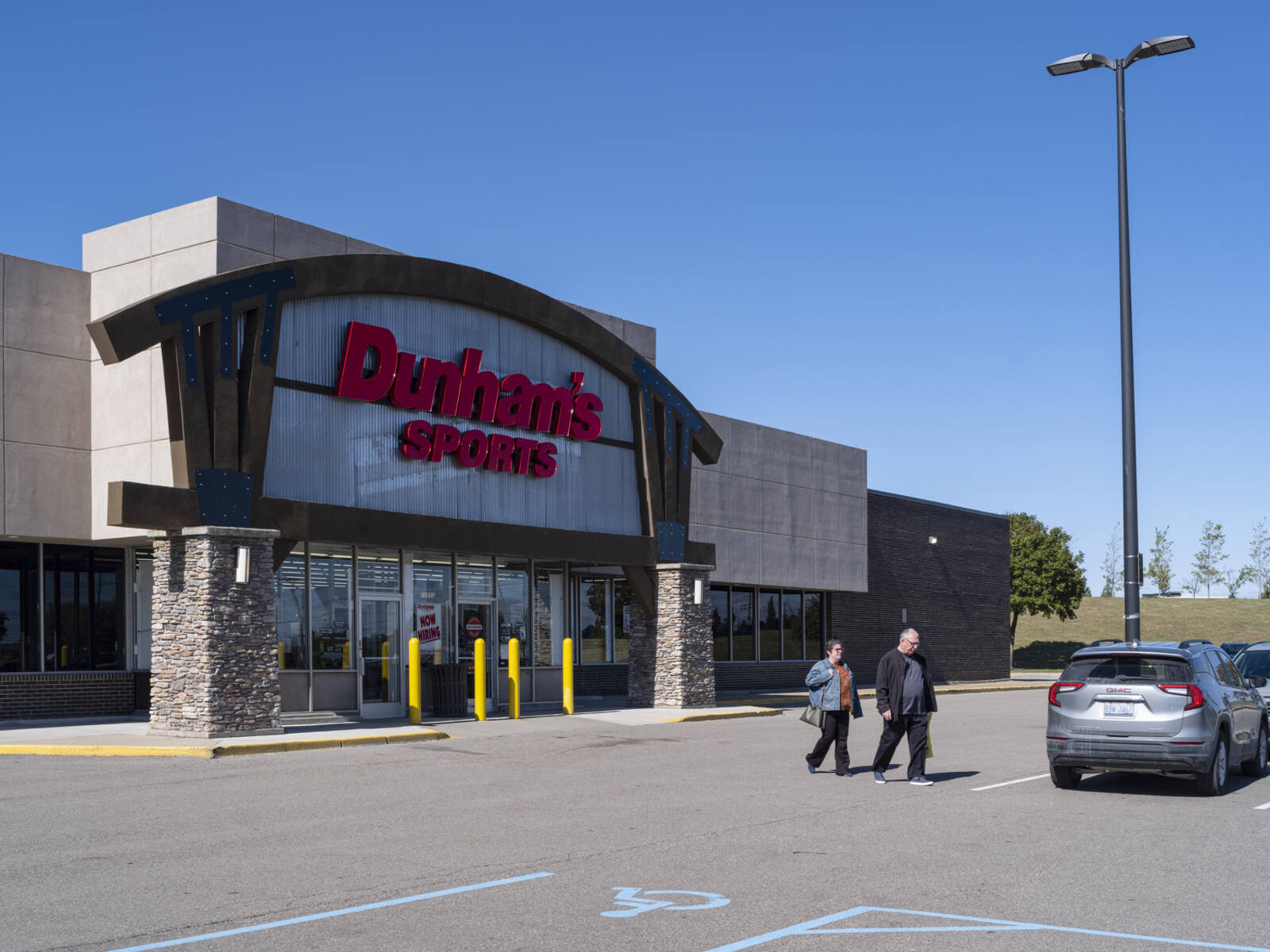 Two people exit Dunham's Sports into parking lot.