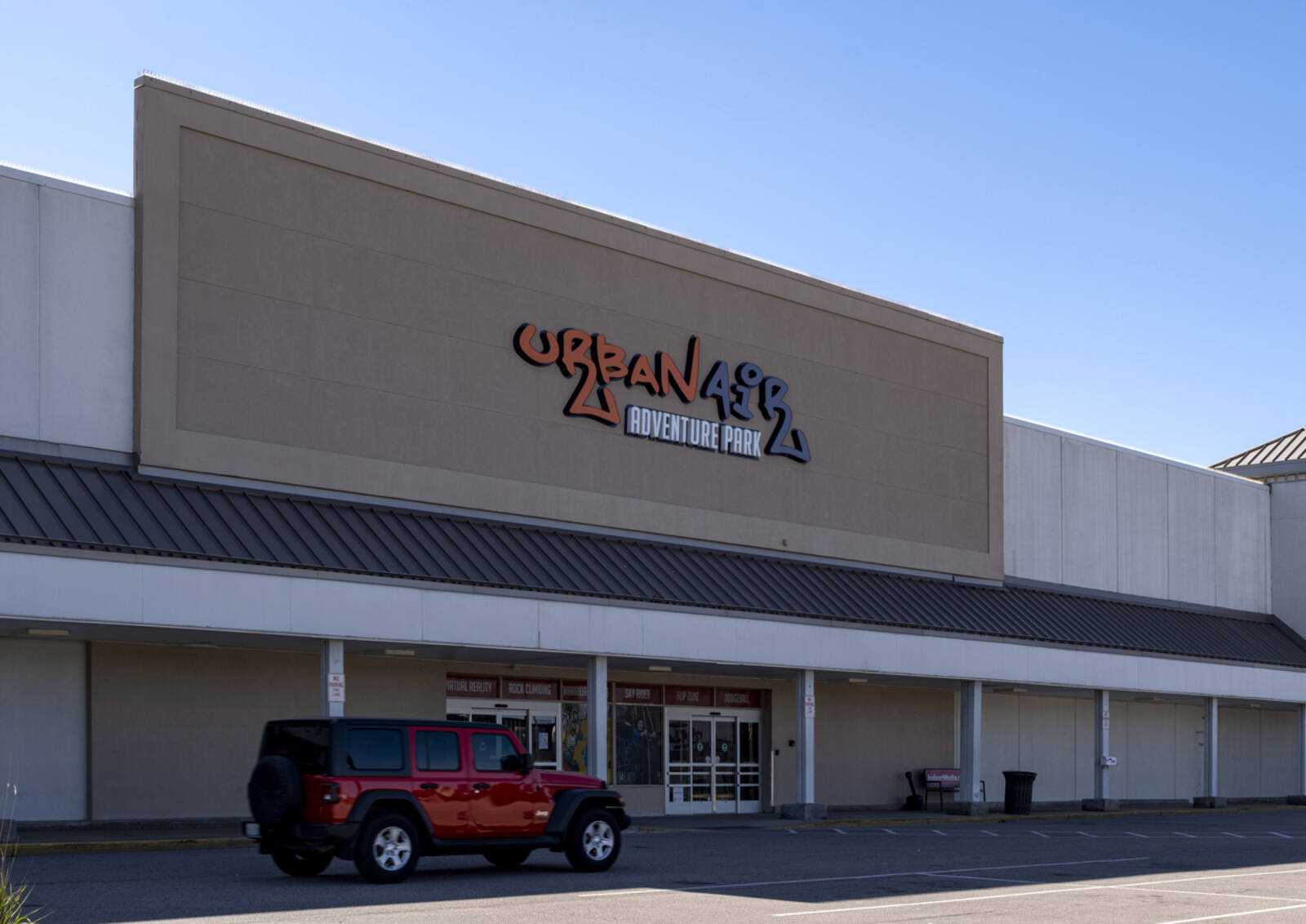 Red Jeep passing façade of Urban Air Adventure Park at Delco Plaza.