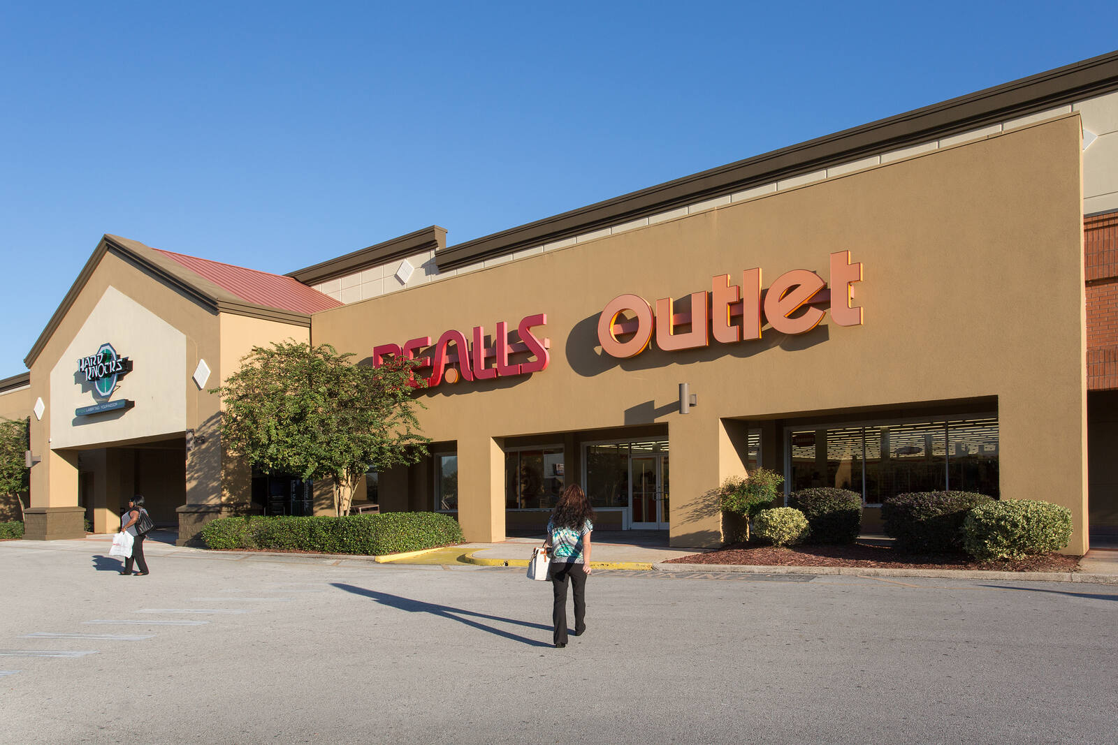 People walking towards Bealls Outlet with a tree in front of entrance on a clear blue sky day